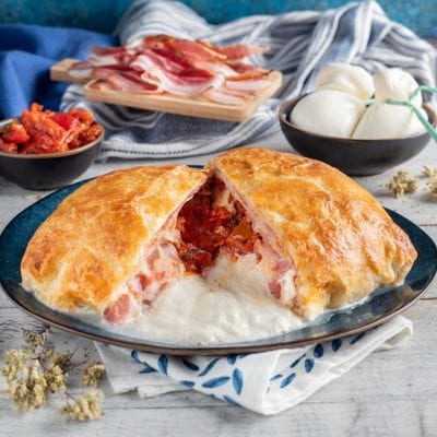 Burrata in crosta sfogliata tagliata a metà con cuore filante, pancetta e pomodori secchi