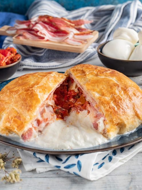 Burrata in crosta sfogliata tagliata a metà con cuore filante, pancetta e pomodori secchi