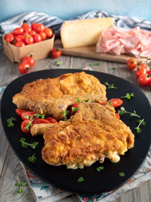 Cotolette alla valdostana impanate e filanti servite con pomodorini e maggiorana fresca
