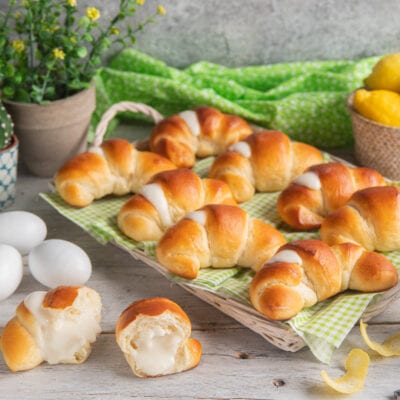 Cornetti soffici allo yogurt dorati e farciti con crema bianca, uno spezzato in primo piano