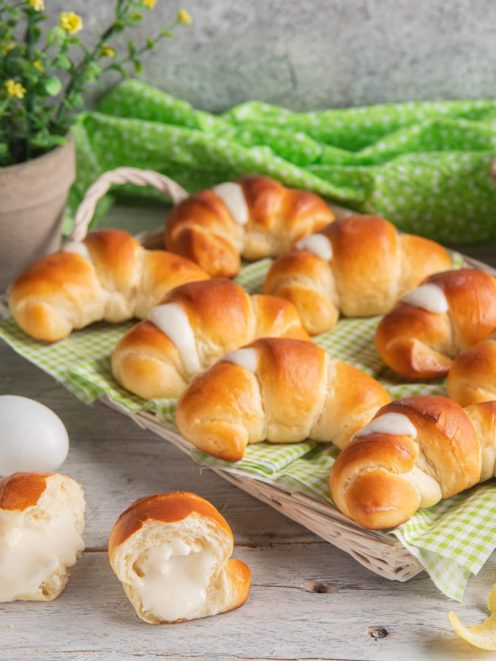 Cornetti soffici allo yogurt dorati e farciti con crema bianca, uno spezzato in primo piano