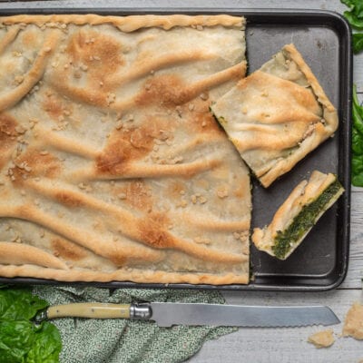 Erbazzone appena sfornato con pasta dorata e croccante, tagliato in porzioni che rivelano il ripieno di erbette verdi
