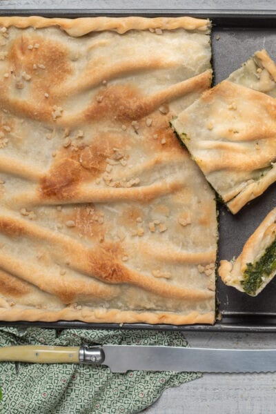 Erbazzone appena sfornato con pasta dorata e croccante, tagliato in porzioni che rivelano il ripieno di erbette verdi