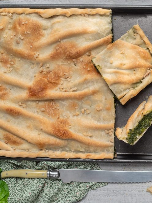 Erbazzone appena sfornato con pasta dorata e croccante, tagliato in porzioni che rivelano il ripieno di erbette verdi