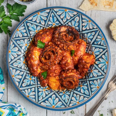 Polpo all'agliata in salsa di pomodoro ricca, guarnito con foglie di prezzemolo fresco