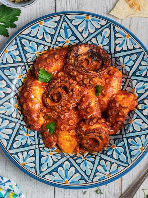 Polpo all'agliata in salsa di pomodoro ricca, guarnito con foglie di prezzemolo fresco