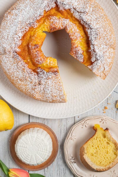 Soffione a ciambella spolverato di zucchero a velo con una fetta a mostrare la mollica soffice al limone