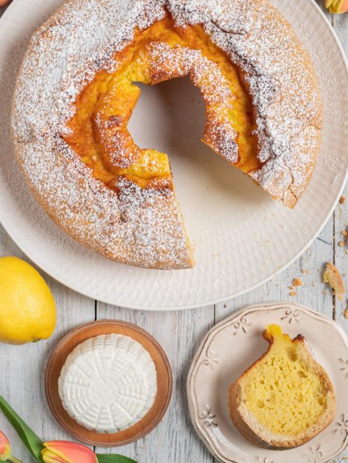 Soffione a ciambella spolverato di zucchero a velo con una fetta a mostrare la mollica soffice al limone