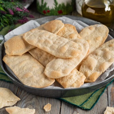 Ciappe croccanti e dorate impilate su carta da forno, con qualche briciola sul tavolo