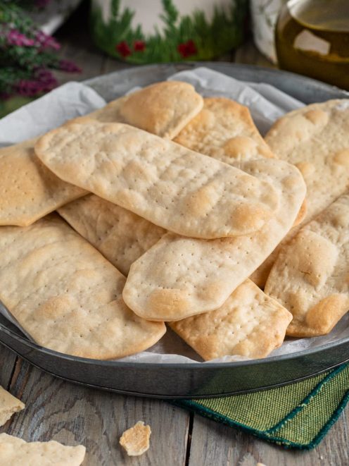 Ciappe croccanti e dorate impilate su carta da forno, con qualche briciola sul tavolo