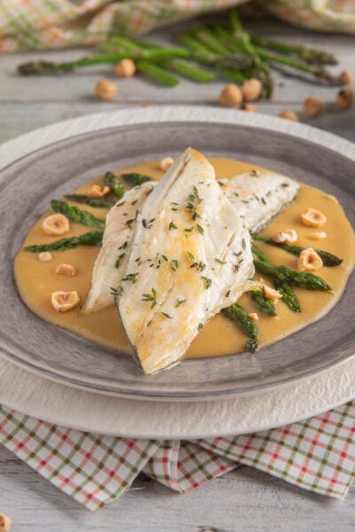 Darna di branzino su salsa dorata con asparagi verdi, nocciole tostate e timo