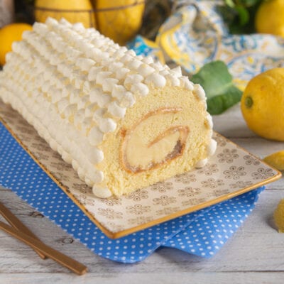 Swiss roll al limone farcito con crema e marmellata, ricoperto di ciuffetti di panna montata