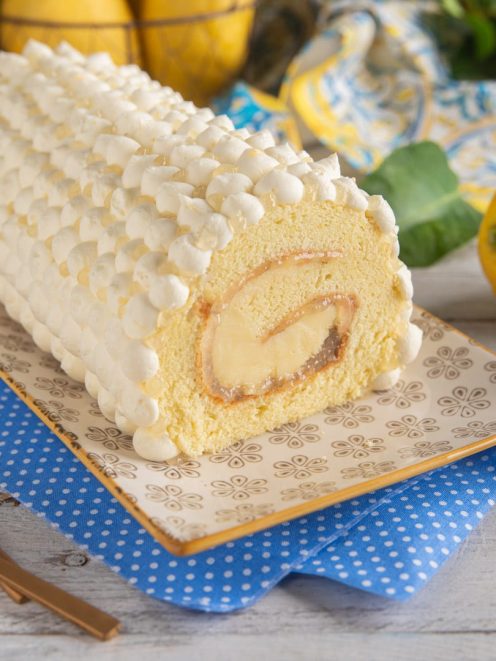 Swiss roll al limone farcito con crema e marmellata, ricoperto di ciuffetti di panna montata