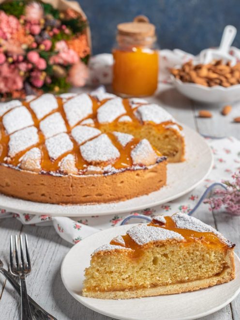 Torta Cremona con zucchero a velo e glassa all'albicocca, una fetta in primo piano che mostra la mollica dorata