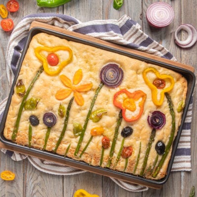 Focaccia primavera decorata con asparagi, peperoni colorati, cipolla rossa e olive a formare fiori e steli