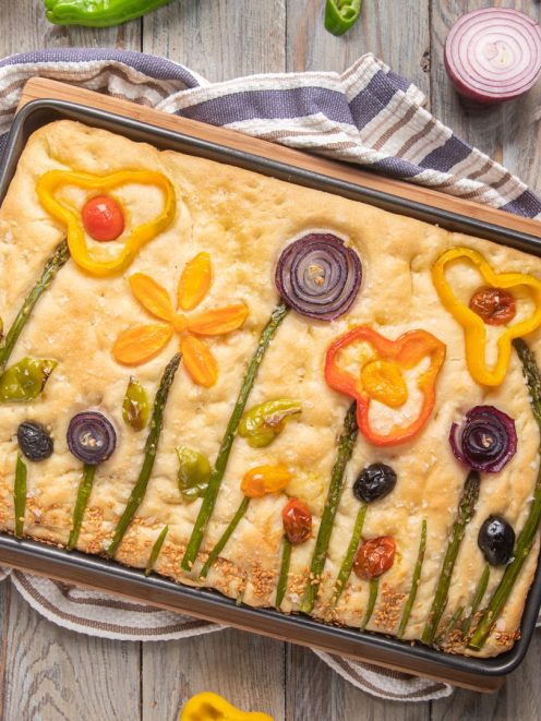 Focaccia primavera decorata con asparagi, peperoni colorati, cipolla rossa e olive a formare fiori e steli