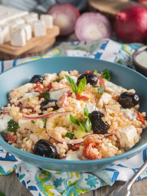 Insalata di riso alla greca con olive nere, feta, pomodori secchi, cetriolo e cipolla rossa