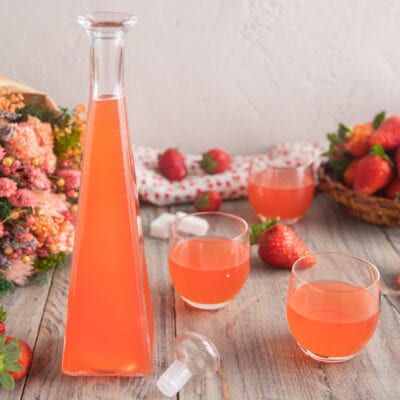 Liquore alla fragola versato in bicchieri, con fragole fresche sullo sfondo
