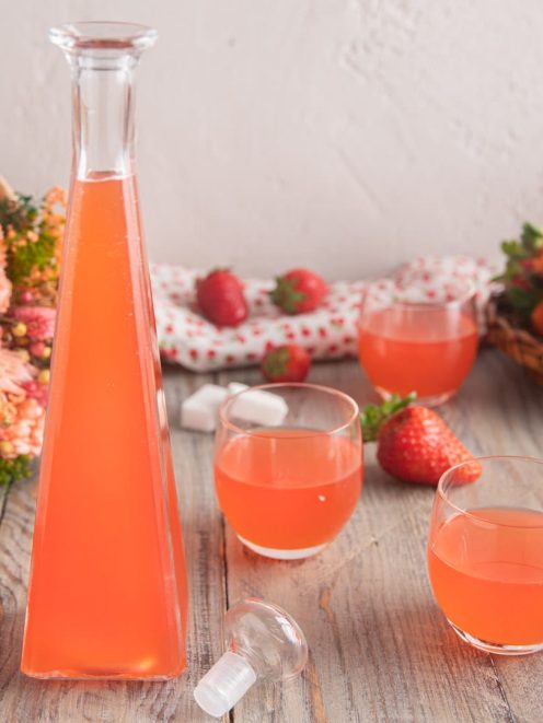 Liquore alla fragola versato in bicchieri, con fragole fresche sullo sfondo