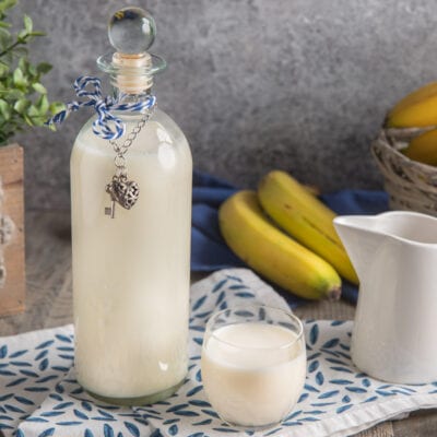 Liquore bananino in bottiglia con tappo di vetro, servito in un bicchiere accanto a banane fresche