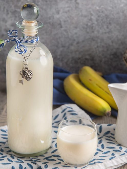 Liquore bananino in bottiglia con tappo di vetro, servito in un bicchiere accanto a banane fresche