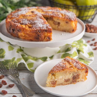 Torta di San Orfeo con mele e uvetta, spolverata di zucchero a velo, con una fetta servita in primo piano