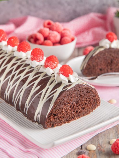 Tronchetto al cioccolato glassato con striature di cioccolato bianco e lamponi freschi su ciuffi di panna