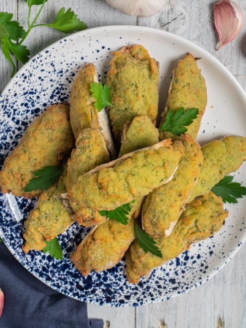 Alici ripiene con crosta verde alle erbe, guarnite con foglie di prezzemolo fresco