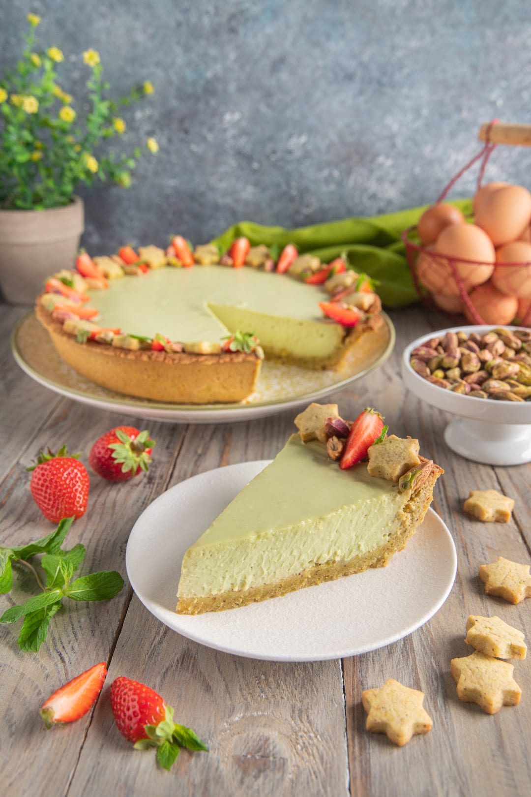 Fetta di crostata al pistacchio e ricotta con fragole e biscottini a stella, torta intera sullo sfondo