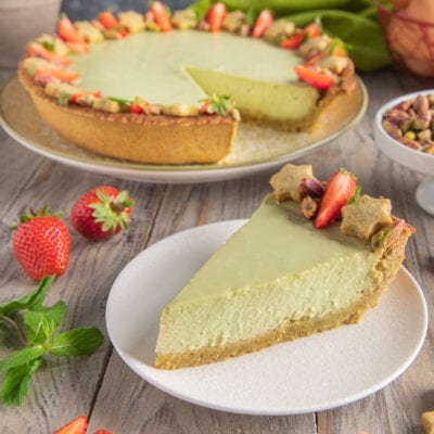 Crostata fredda al pistacchio e ricotta con una fetta servita, guarnita da fragole e pistacchi
