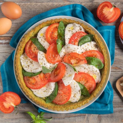 Crostata salata caprese con fette di pomodoro, mozzarella e basilico fresco a spirale