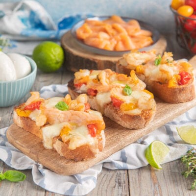 Crostone con mozzarella, gamberi e pomodorini gratinati, guarnito con foglie di basilico fresco