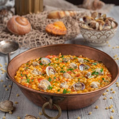 Fregola con le arselle in tegame di rame, con pomodoro e prezzemolo tritato