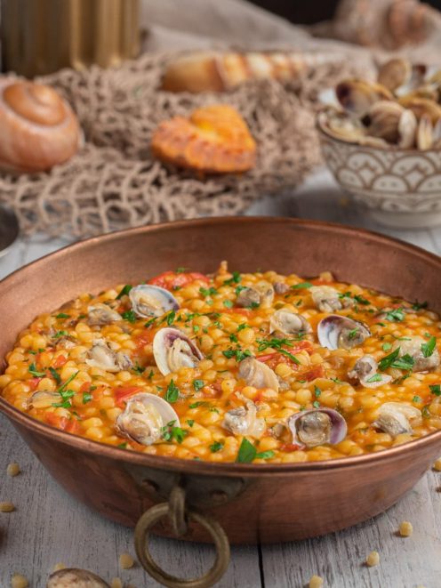 Fregola con le arselle in tegame di rame, con pomodoro e prezzemolo tritato