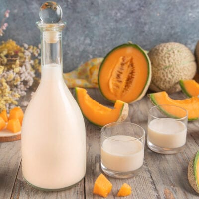 Meloncello cremoso servito in due bicchieri accanto a fette e cubetti di melone cantalupo