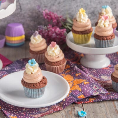 Mini cupcake ai tre cioccolati con frosting rosa e fiori di zucchero colorati