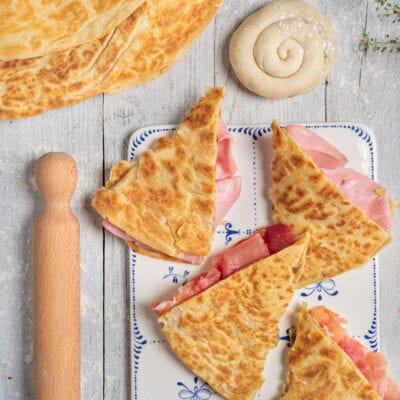 Crescia sfogliata tagliata a spicchi e farcita con prosciutto cotto, servita con un panetto di pasta arrotolata