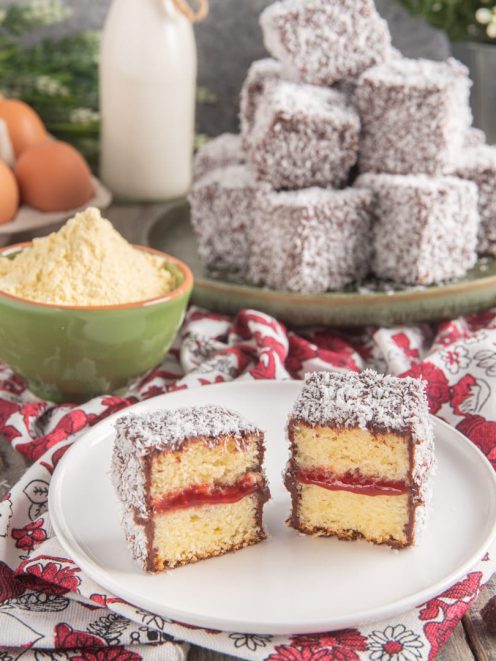 Lamingtons tagliati a metà con strato di confettura, glassa al cioccolato e cocco grattugiato