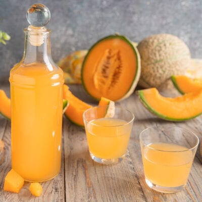 Liquore al melone servito in bottiglia e due bicchieri, con fette di melone cantalupo sullo sfondo