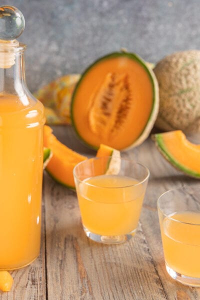 Liquore al melone servito in bottiglia e due bicchieri, con fette di melone cantalupo sullo sfondo