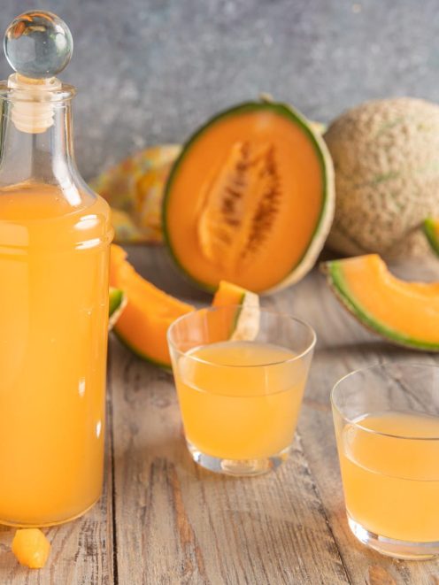 Liquore al melone servito in bottiglia e due bicchieri, con fette di melone cantalupo sullo sfondo