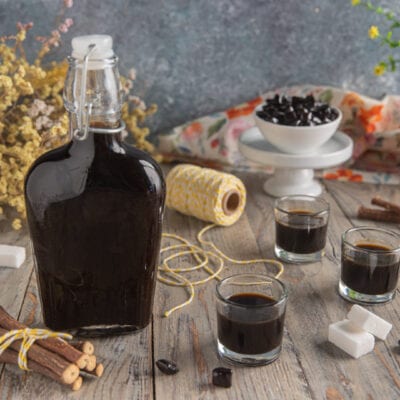 Liquore alla liquirizia in bottiglia con tre bicchierini, radici di liquirizia e zucchero a cubetti