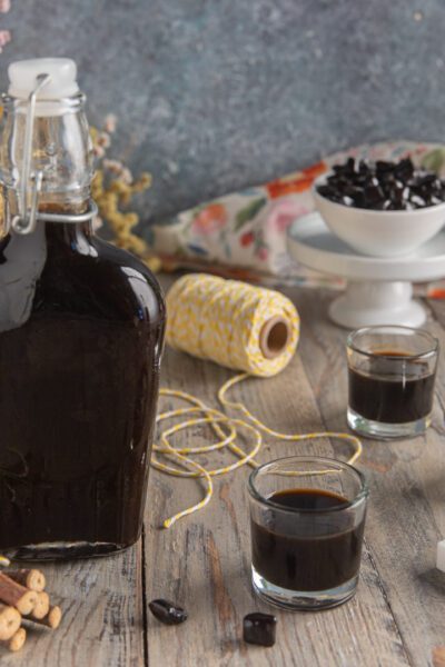 Liquore alla liquirizia in bottiglia con tre bicchierini, radici di liquirizia e zucchero a cubetti