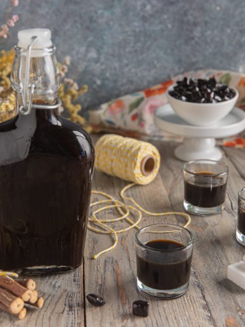 Liquore alla liquirizia in bottiglia con tre bicchierini, radici di liquirizia e zucchero a cubetti