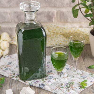Liquore alla menta versato in due bicchieri da liquore, con la bottiglia accanto