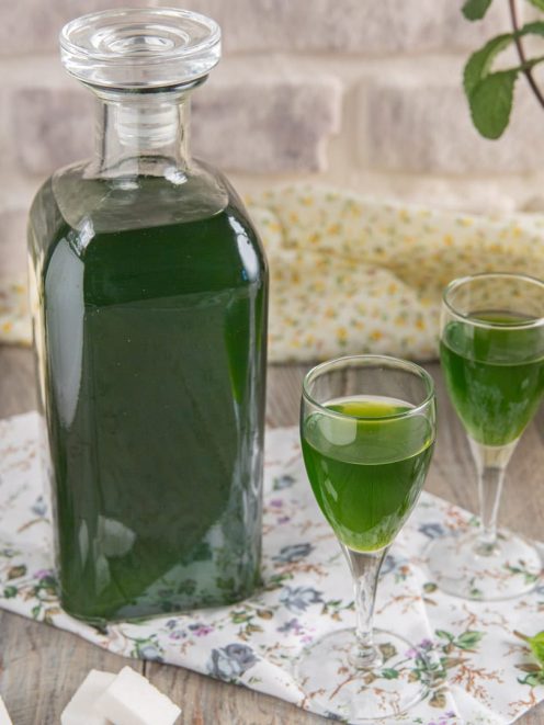 Liquore alla menta versato in due bicchieri da liquore, con la bottiglia accanto