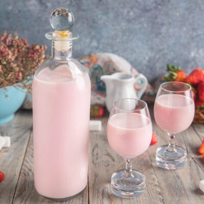 Liquore panna e fragola servito in due calici con fragole fresche sullo sfondo