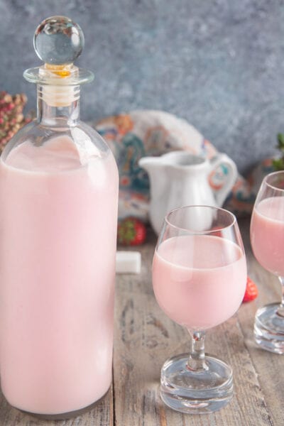 Liquore panna e fragola servito in due calici con fragole fresche sullo sfondo