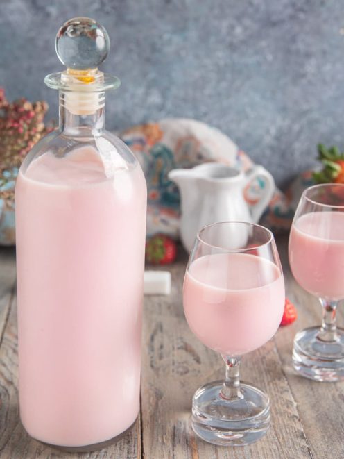 Liquore panna e fragola servito in due calici con fragole fresche sullo sfondo