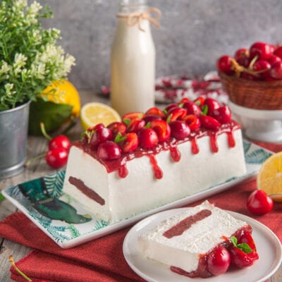 Mattonella allo yogurt e ciliegie con coulis rosso che cola sui lati e una fetta servita a parte